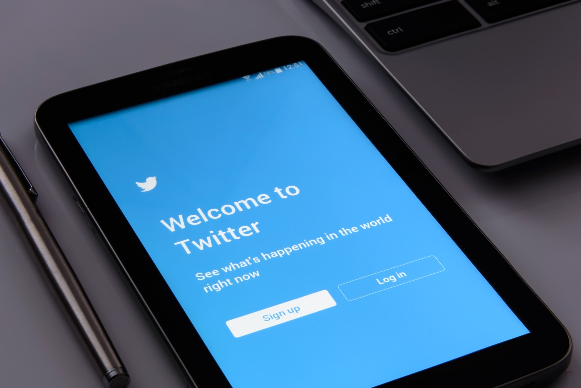 Twitter Welcome screen on a smartphone, in the center of a pen and laptop. With the Signup and Login button the screen