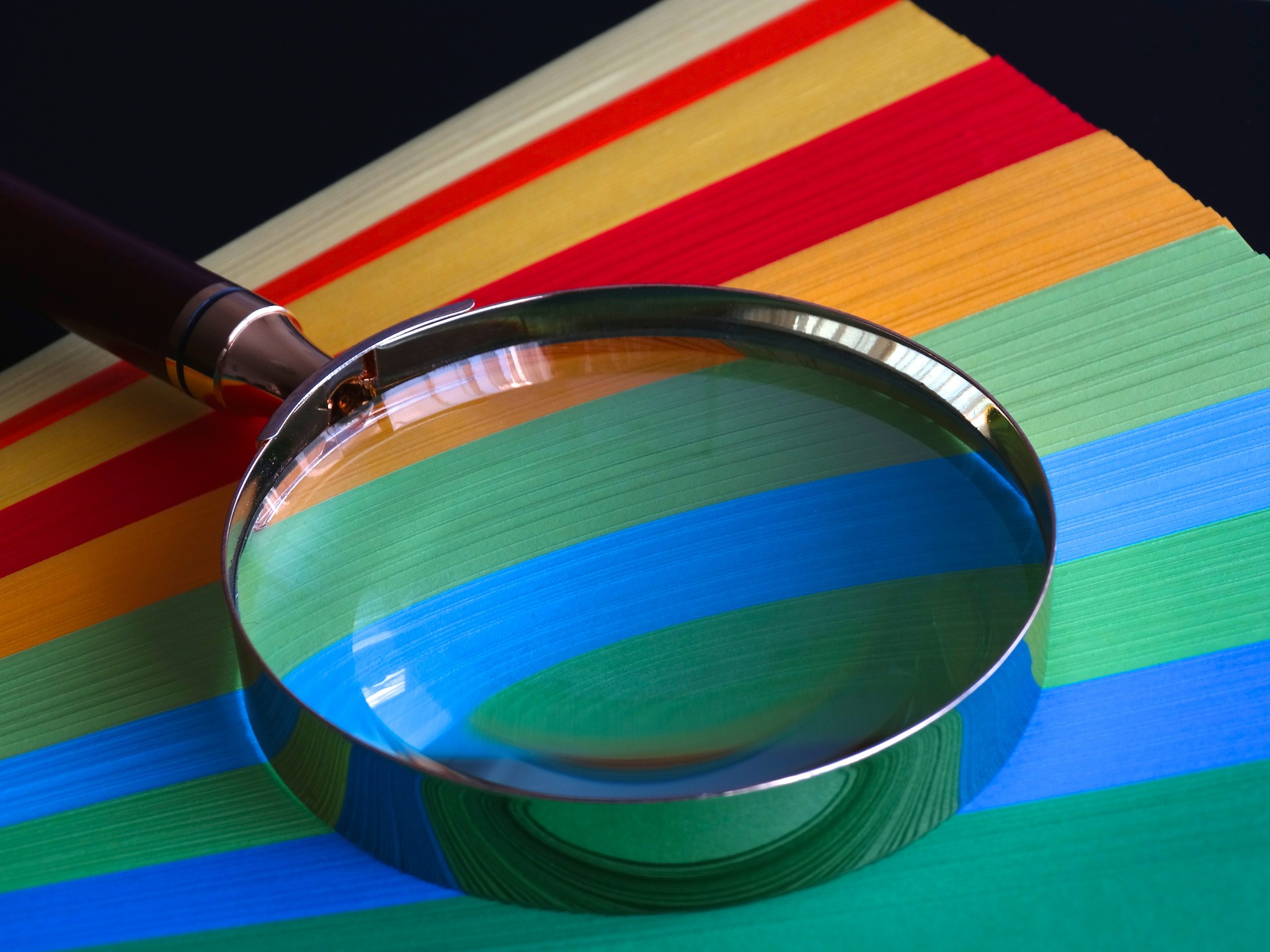 A magnifying glass on top of rainbow colored papers, indicating the various forms of micro influencer promotion platforms that are there to look at